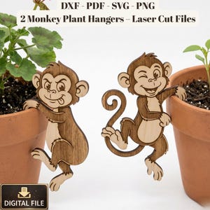 May include: Two laser-cut wooden monkey plant hangers. The monkeys are brown with light wood accents, winking and sticking out their tongues. The text "DXF - PDF - SVG - PNG" and "2 Monkey Plant Hangers - Laser Cut Files" are at the top. A "DIGITAL FILE" icon is at the bottom.