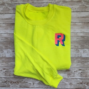 May include: A neon yellow sweatshirt with a large, pink and blue "R" on the front.