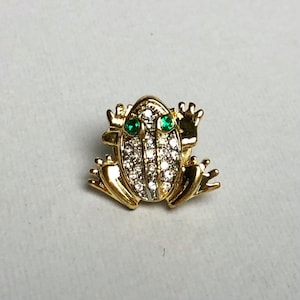 May include: A gold-tone frog brooch with green rhinestone eyes and a body covered in clear rhinestones.