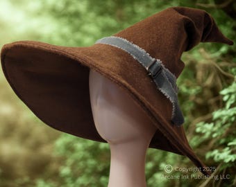 May include: A brown pointed hat with a wide brim and a grey fabric band featuring frayed edges and a metal buckle. The hat is displayed on a mannequin head. The text Copyright 2025 Arcane Ink Publishing LLC is visible in the bottom right corner.