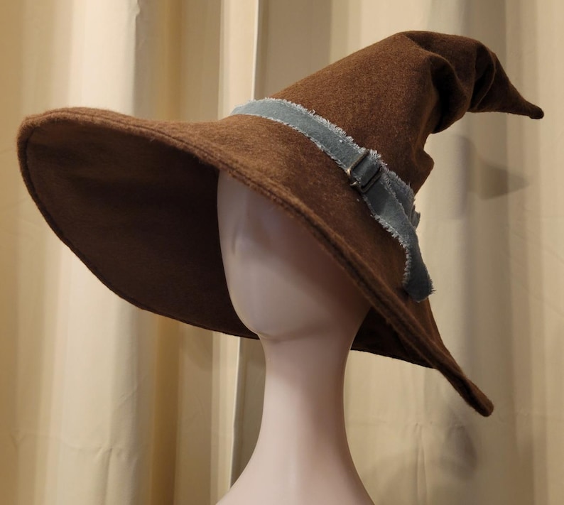 May include: A brown felt wizard hat with a wide brim and a pointed crown. The hat has a blue denim band with a buckle.