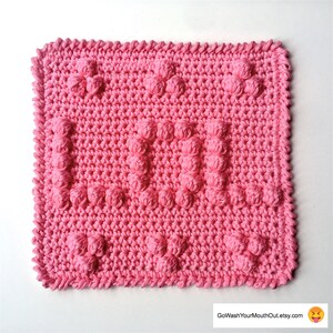 May include: A pink crocheted dishcloth with a textured, bumpy design. The dishcloth is square shaped and has a fringed edge.