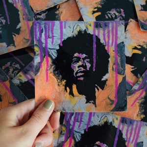 May include: A close-up of a sticker featuring a black and white portrait of Jimi Hendrix with a purple and orange abstract background.