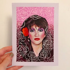 May include: A painting of a woman with dark hair and purple eyeshadow. She is wearing a dark shirt and has a red flower behind her ear. The background is pink with white outlines of roses.