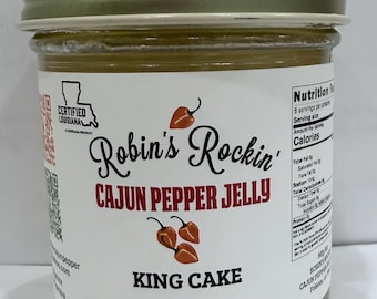 May include: A glass jar of Robin's Rockin' Cajun Pepper Jelly King Cake flavor with a gold metal lid. The white label features red text, illustrations of three orange peppers, a Certified Louisiana logo, and a nutrition facts panel. Net wt. 8 oz.