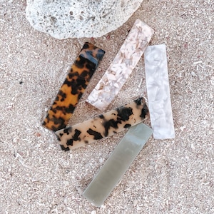 May include: Five hair clips in different colors and patterns. The clips are made of plastic and have a rectangular shape. The colors include brown, white, and gray.