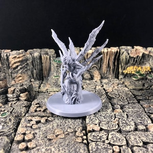 Puede incluir: Una miniatura gris y detallada de una criatura con alas y un cuerpo nudoso parecido a un árbol. La miniatura está sobre una base gris y se coloca sobre una superficie de piedra.