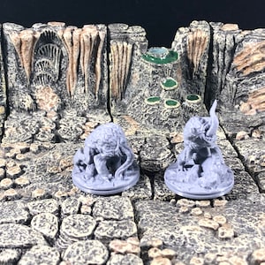 May include: Two gray, 3D printed miniature figures of creatures with multiple legs and tentacles. The figures are standing on round bases. The figures are on a gray, textured surface.