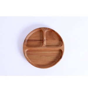 May include: A round wooden serving tray with three divided sections. The tray is made of light brown wood and has a smooth finish.