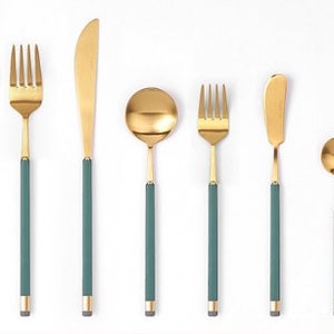 May include: A set of gold-toned cutlery with green handles. The set includes a fork, knife, spoon, and chopsticks.