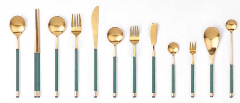 May include: A set of gold-toned cutlery with green handles. The set includes a fork, knife, spoon, and chopsticks.