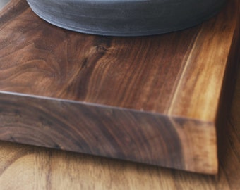 May include: A white ceramic mug with a handle sits on a dark gray ceramic tray with a folded pink cloth napkin. The tray is on a wooden surface.