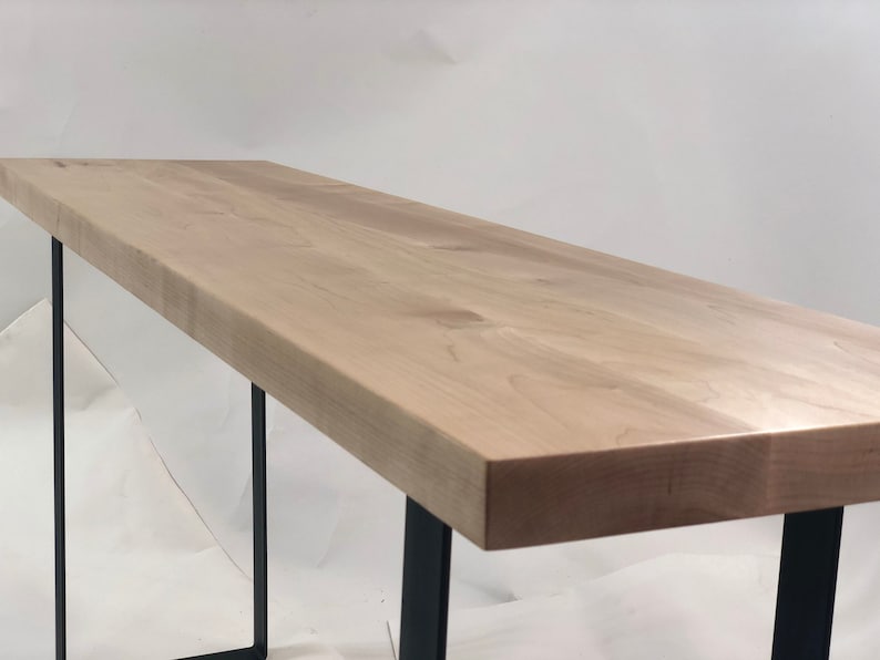 May include: A long, rectangular wooden table with a natural wood finish and black metal legs. The table top is smooth and has a slight grain pattern.