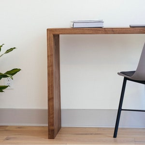 May include: A wooden desk with a gray chair. The desk has a simple design with a rectangular top and a single shelf. The chair has a curved back and black metal legs.