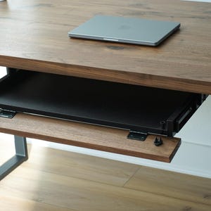 May include: A wooden desk with a pull-out keyboard tray and a laptop on top. The desk has a dark brown finish and a black metal frame. The keyboard tray is made of wood and black metal.