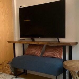 May include: A dark wood console table with a black metal frame and a blue upholstered bench underneath. The table has a flat top surface and is supporting a flat screen television.