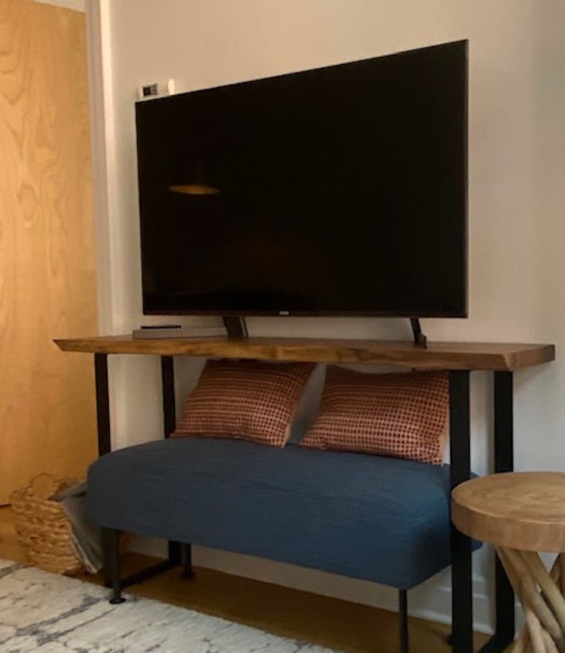 May include: A dark wood console table with a black metal frame and a blue upholstered bench underneath. The table has a flat top surface and is supporting a flat screen television.