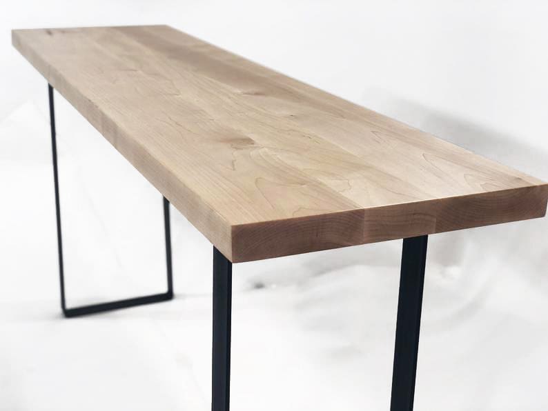 May include: A long, narrow table with a light wood top and black metal legs. The table is made of solid wood and has a simple, modern design.