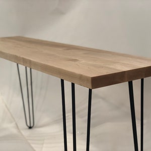 May include: A light wood console table with four black hairpin legs.