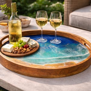 Puede incluir: Una bandeja de madera redonda con un diseño de océano azul y blanco, que contiene copas de vino, una botella de vino y un plato de aperitivos. La bandeja tiene asas y está sobre una mesa.