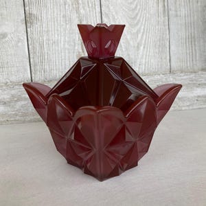 May include: A burgundy glass candy dish with a geometric design and a matching lid shaped like a flower.