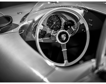 Op de afbeelding: Zwart-witfoto van het interieur van een oldtimer, met een close-up van het stuurwiel met een Porsche-logo in het midden.