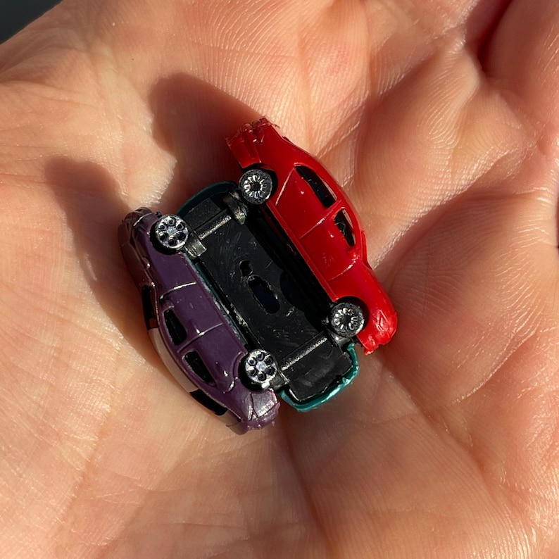 May include: Three toy cars stacked on top of each other. The top car is red, the middle car is green, and the bottom car is purple.