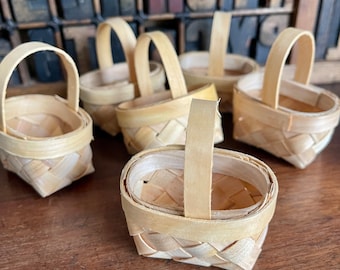 May include: A set of six small, woven baskets with handles. The baskets are made of natural, light brown material and have a simple, rustic design.