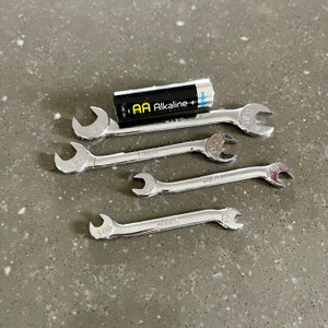 May include: Five silver wrenches with black markings, including 5/16, 7/16, 1/2, 9/16, and 5/8, and a single AA alkaline battery.