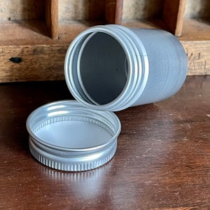 May include: A silver metal container with a white lid. The container is open and the lid is sitting next to it.
