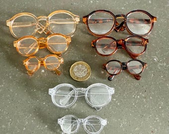 May include: A set of eight pairs of glasses in various sizes and colors, including clear, brown, and amber. The glasses are arranged in a row from largest to smallest, with a British one pound coin in the middle.