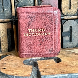 May include: A small, red leather-bound book with the title "THUMB DICTIONARY" embossed in gold lettering.