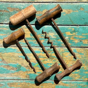 May include: Several antique corkscrews are displayed, each with a wooden handle and a metal spiral. The corkscrews have different designs, including T-shaped and spiral styles. The wood has a warm, aged look, and the metal shows signs of wear and use.
