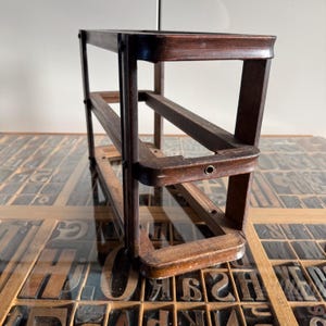 May include: A rectangular dark brown wooden frame structure featuring four vertical corner posts connected by horizontal rails. The frame has a smooth finish with visible wood grain and small metal rivets securing the joints at each corner.
