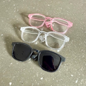 May include: Three pairs of glasses, one black, one clear, and one pink. The glasses are all rectangular in shape and have a modern design.
