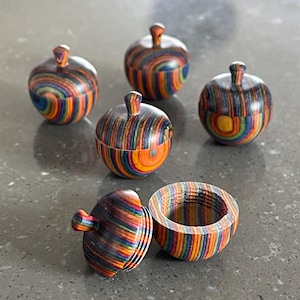 May include: Five small wooden boxes with lids, each with a different rainbow-colored wood grain pattern. The boxes are round and have a small knob on top. One box is open, revealing the inside.