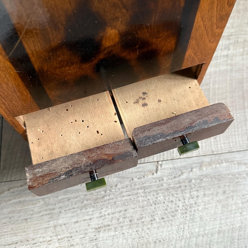 May include: Close-up of a vintage wooden cabinet with two drawers partially open. The cabinet has a dark wood finish with black accents. The drawer pulls are green and square. The drawers are made of light-colored wood.