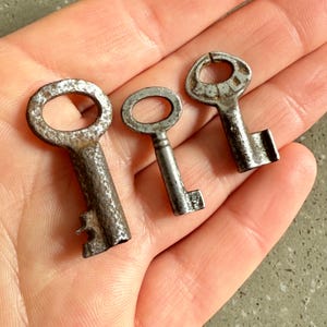 Könnte beinhalten: Drei antike Schlüssel mit unterschiedlichen Designs und Oberflächen. Die Schlüssel sind aus Metall und haben ein abgenutztes, altes Aussehen.