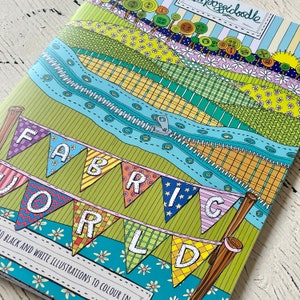 May include: A colouring book cover with a colourful illustration of a fabric world. The cover features a banner with the words "FABRIC WORLD" and a zipper design.