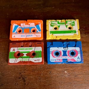 May include: Four colourful cassette tape shaped puzzles with different designs. The tapes are labelled "Big Eagle", "Power Lion King", "Warrior", and "Wing Bird". Each tape has a side A and a side B and is labelled "MC90".