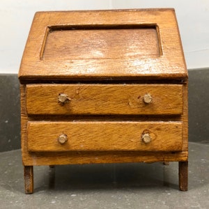 Peut inclure: Un petit bureau en bois avec un dessus incliné et deux tiroirs. Le bureau est peint en brun clair et a de simples boutons en bois.