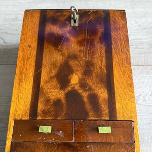 May include: A vintage wooden desk with a keyhole and two small drawers. The desk is made of dark and light brown wood with a glossy finish. The drawer pulls are a light green color.