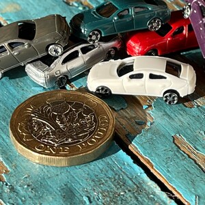 May include: A close-up of a British one pound coin with a floral design. The coin is lying on a blue and white painted wooden surface with several toy cars scattered around it.