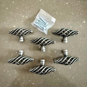 May include: A set of six silver-finished cabinet knobs with a distinctive cage design. The image also shows a small bag of screws. These decorative knobs are designed for easy fitting and will add a touch of elegance to any furniture.