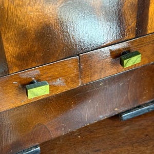 May include: Close-up of a wooden cabinet with a glossy, dark brown finish. The cabinet features two small, rectangular green and black knobs. The wood grain is visible, and the overall aesthetic is vintage.
