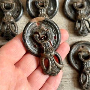 May include: Close-up of several antique bronze drawer pulls. Each pull features a circular backplate with a decorative design and a curved handle. The pulls have a weathered, aged appearance, suggesting they are vintage or vintage-inspired.