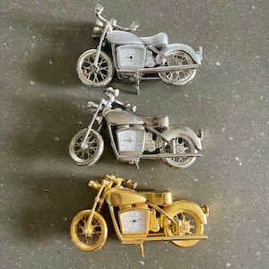 Könnte beinhalten: Drei Miniatur-Motorrad-Uhren, eine silberne, eine goldene und eine verchromte. Jede Uhr verfügt über ein detailliertes Design und ein funktionierendes Zifferblatt.