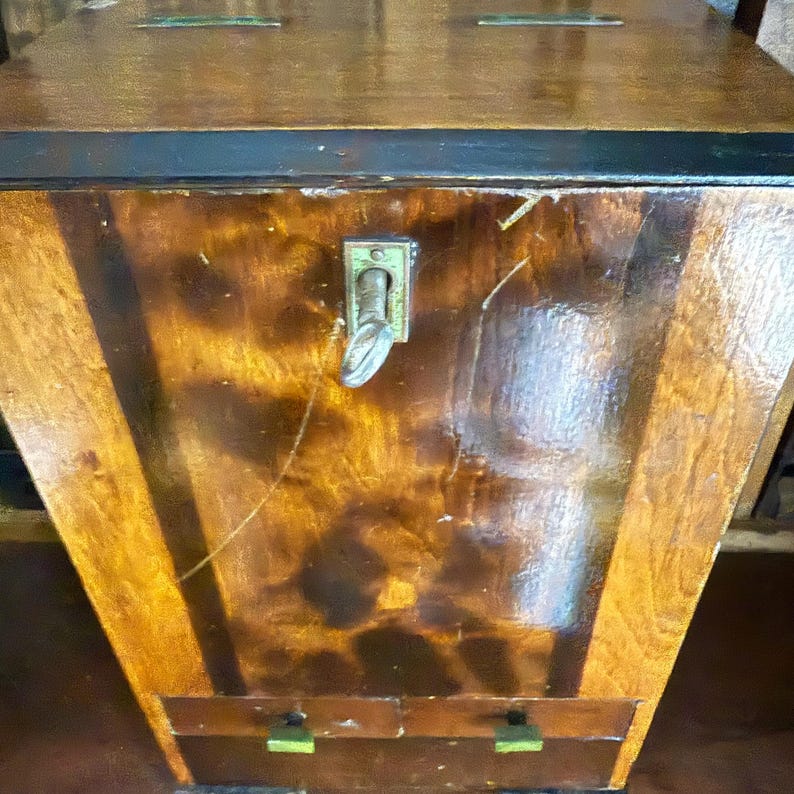 May include: A vintage wooden chest with a glossy finish. The chest features a dark brown top and a lighter brown body with vertical wood grain. It has a metal latch and two small drawers at the bottom with green accents.