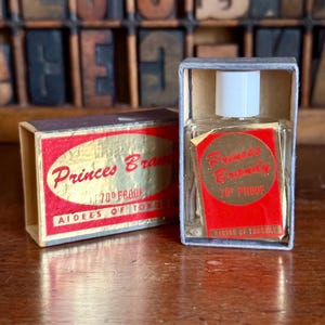 May include: A vintage bottle of Princes Brandy, 70 proof, in a small box. The box is red and gold with the brand name in a script font. The bottle is clear with a white cap and a red label.