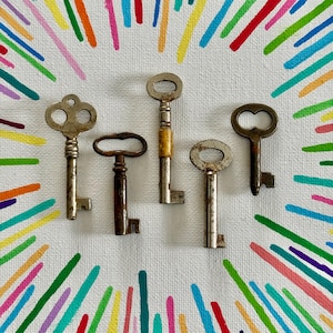 Könnte beinhalten: Fünf antike Bartschlüssel in verschiedenen Größen und Designs sind auf einer weißen Leinwand angeordnet. Die Schlüssel sind aus Metall und weisen Gebrauchsspuren auf. Der Hintergrund zeigt farbenfrohe, strahlenförmige Pinselstriche.